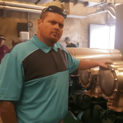 A man in blue shirt standing next to pipes.